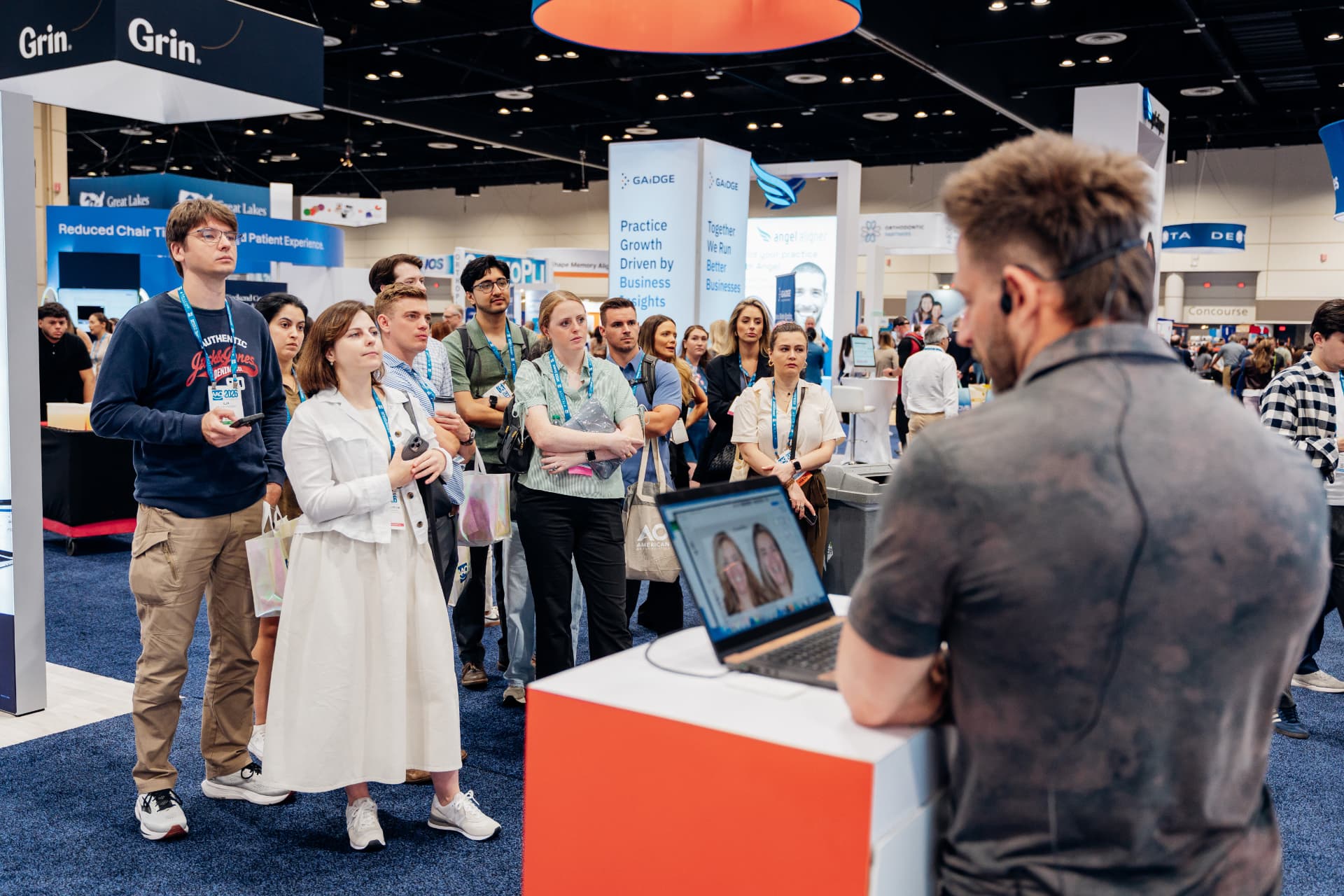 Corporate event photography of attendees gathered at an exhibitor booth demonstration on a trade show floor